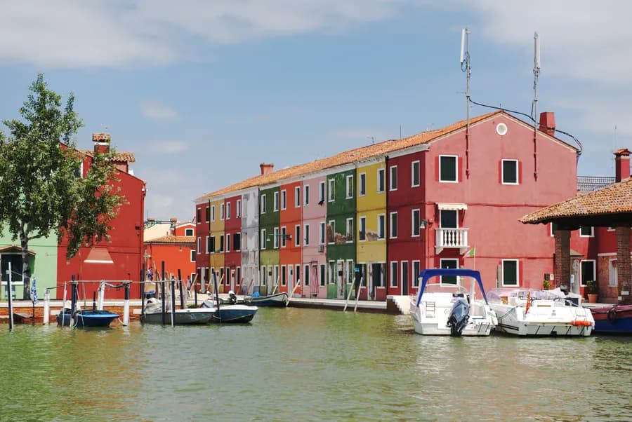 View approaching a canal in Burano, Italy with anchored boats and a row colorful buildings