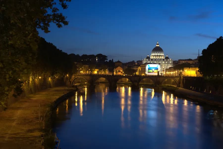 the St. Peter's Basilica seen at night from across the Tiber River in Rome