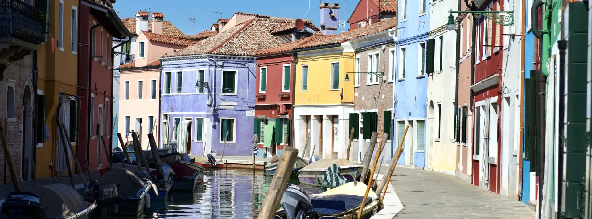 View looking up a canal with anchored boats and colorful buildings in Burano, Italy