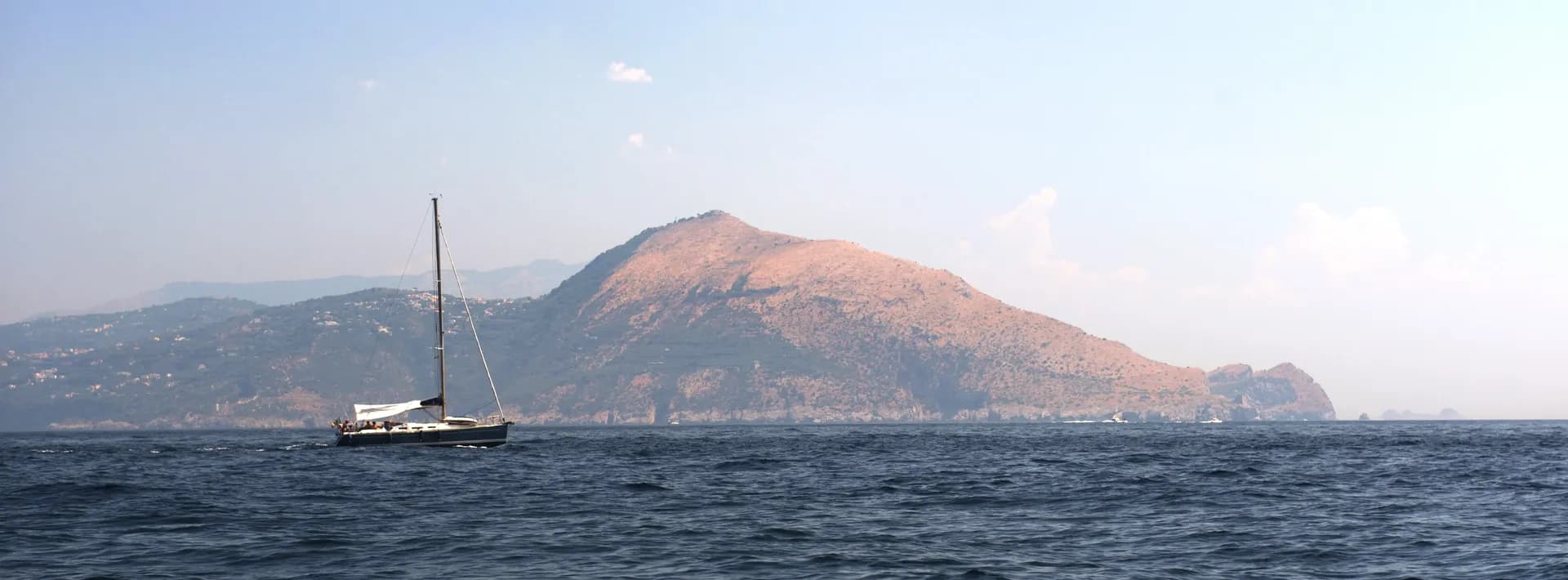 view from the water of a mountain with sailboat in foreground in Capri, Italy