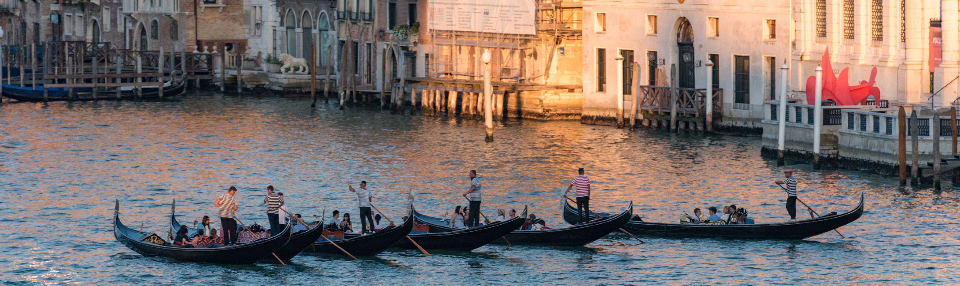 Row of passenger-filled gondolas crossing the Grand Canal at sunset