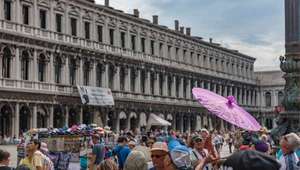 Piazza San Marco filled with visitors, flanked by arches of loggia
